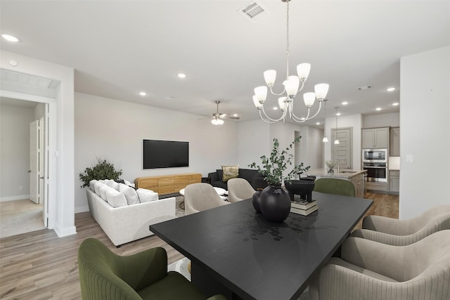 dining space with ceiling fan with notable chandelier and light wood-type flooring