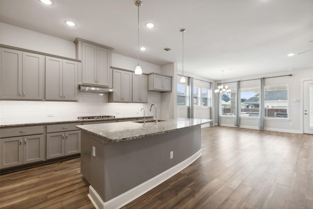 kitchen featuring sink, light stone counters, pendant lighting, a kitchen island with sink, and decorative backsplash