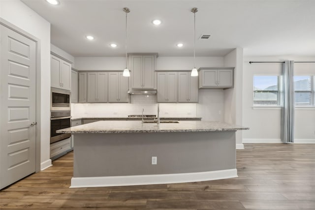 kitchen featuring sink, decorative light fixtures, a center island with sink, stainless steel appliances, and light stone countertops