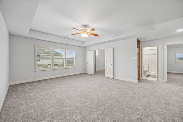 unfurnished bedroom featuring light carpet, a tray ceiling, ensuite bath, and ceiling fan