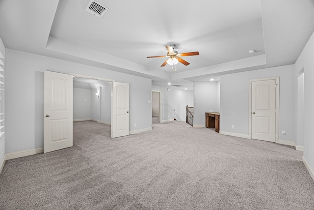 unfurnished living room with light carpet, a raised ceiling, and ceiling fan