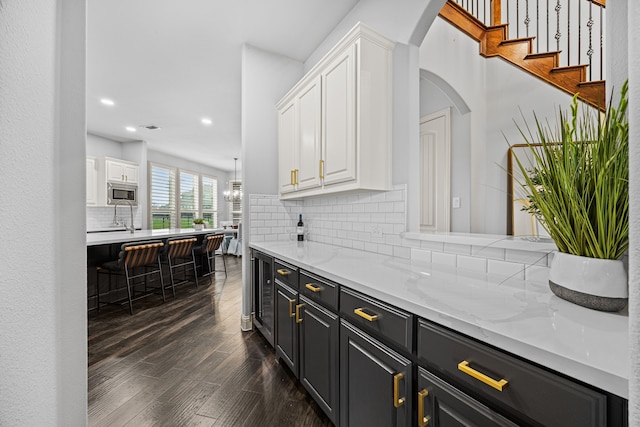 bar with tasteful backsplash, dark hardwood / wood-style flooring, stainless steel microwave, and white cabinets