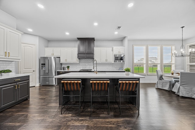 kitchen with backsplash, a kitchen island with sink, white cabinets, dark hardwood / wood-style floors, and stainless steel appliances