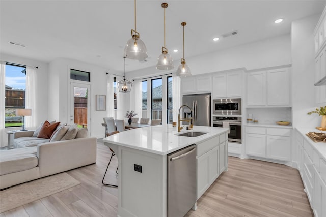 kitchen featuring light countertops, appliances with stainless steel finishes, open floor plan, a kitchen island with sink, and white cabinetry