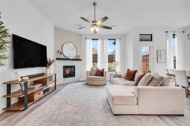 living room with light wood-style floors, ceiling fan, a fireplace, and visible vents