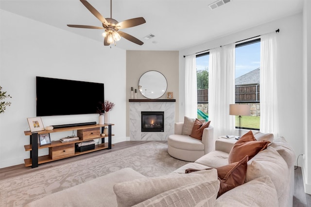 living room with a high end fireplace, light hardwood / wood-style floors, and ceiling fan