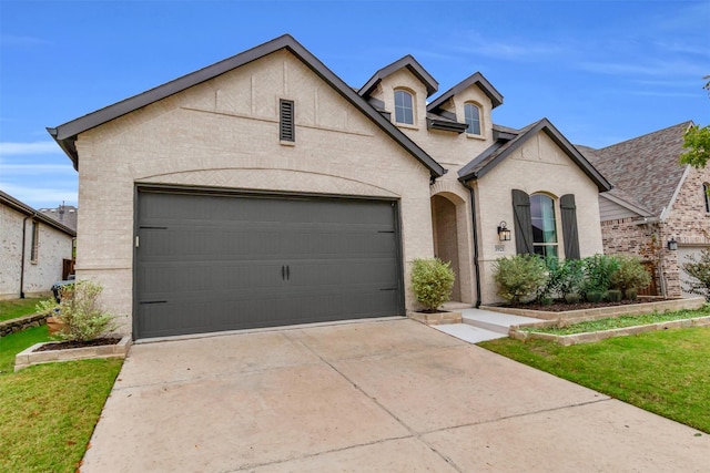 french country inspired facade featuring driveway, brick siding, an attached garage, and a front yard