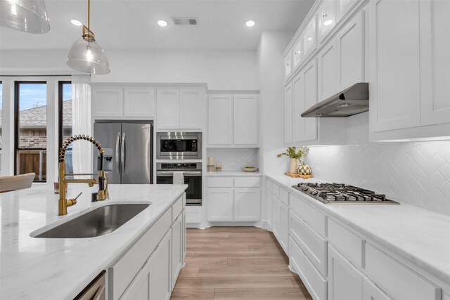 kitchen featuring an island with sink, decorative light fixtures, light hardwood / wood-style floors, white cabinetry, and stainless steel appliances