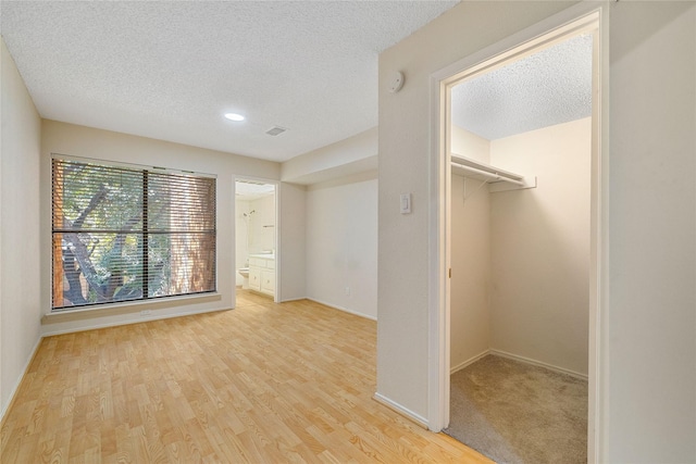 unfurnished bedroom featuring a walk in closet, ensuite bathroom, a textured ceiling, and light wood-type flooring