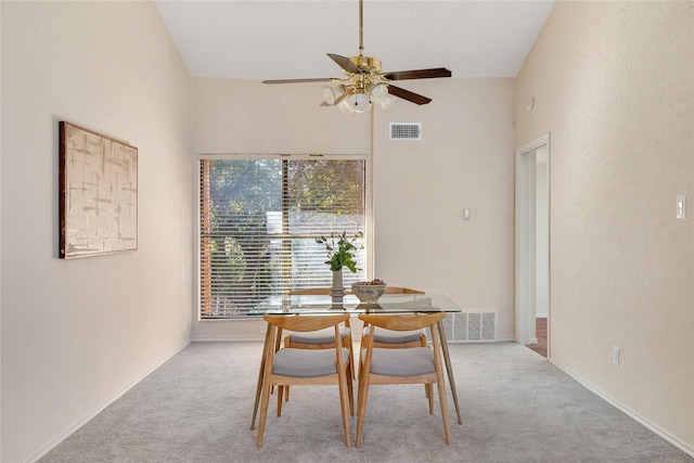 dining room with light carpet, ceiling fan, and a high ceiling