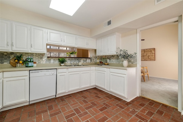 kitchen with a skylight, dishwasher, sink, white cabinets, and backsplash