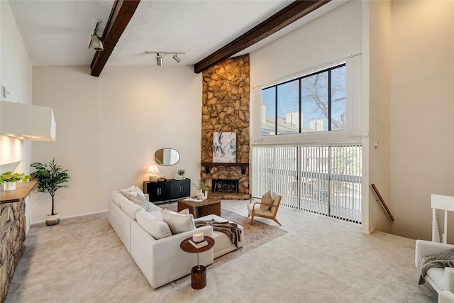 living room featuring beam ceiling, a stone fireplace, light carpet, and track lighting