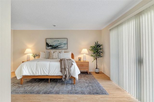 bedroom with a textured ceiling, light hardwood / wood-style flooring, and ornamental molding