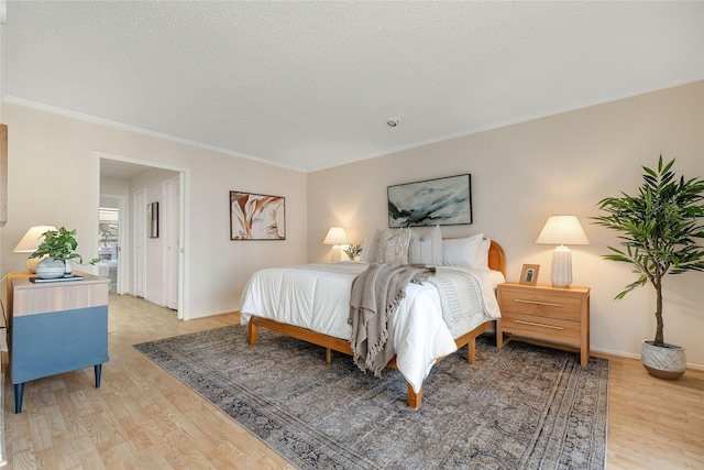 bedroom with crown molding, a textured ceiling, and light wood-type flooring