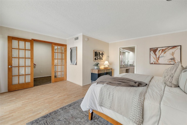 bedroom featuring a textured ceiling, ornamental molding, light hardwood / wood-style flooring, and french doors