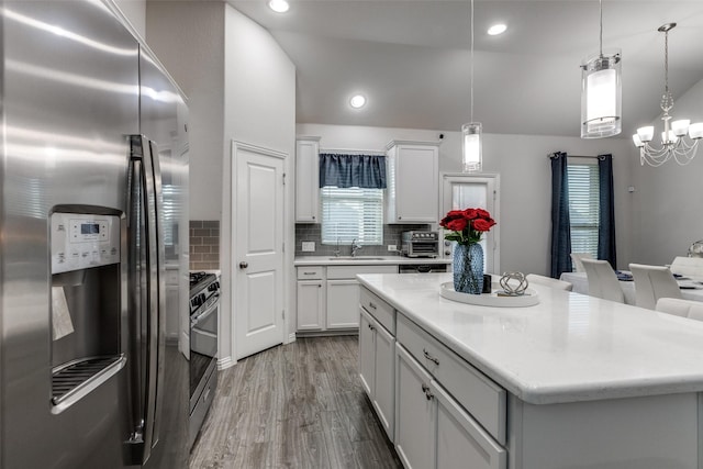 kitchen featuring white cabinetry, stainless steel appliances, hanging light fixtures, and decorative backsplash