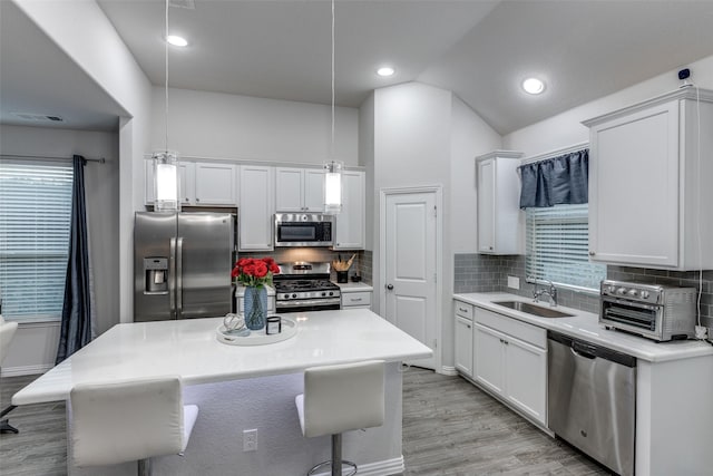 kitchen with pendant lighting, sink, appliances with stainless steel finishes, white cabinets, and vaulted ceiling