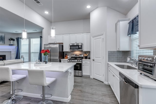 kitchen with sink, decorative light fixtures, appliances with stainless steel finishes, light hardwood / wood-style floors, and white cabinets