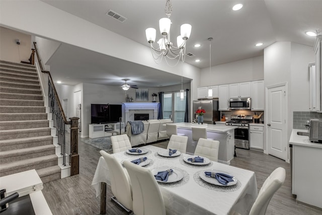 dining area featuring hardwood / wood-style floors, a high ceiling, ceiling fan with notable chandelier, and a fireplace