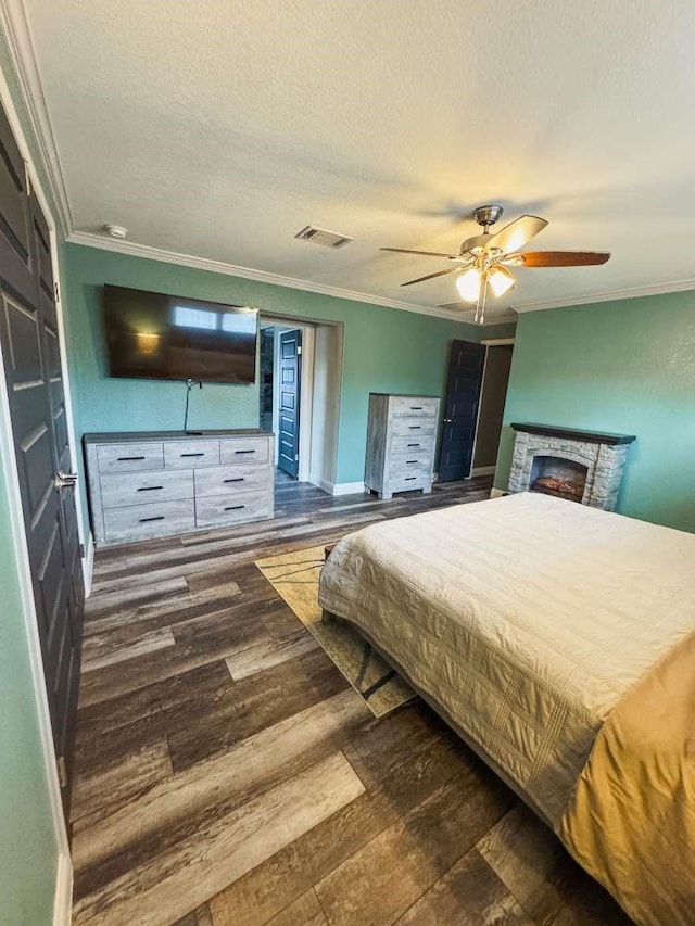 bedroom featuring ceiling fan, dark wood-type flooring, a stone fireplace, and ornamental molding