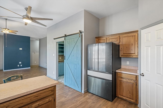 kitchen featuring stainless steel fridge, ceiling fan, a barn door, and light hardwood / wood-style flooring