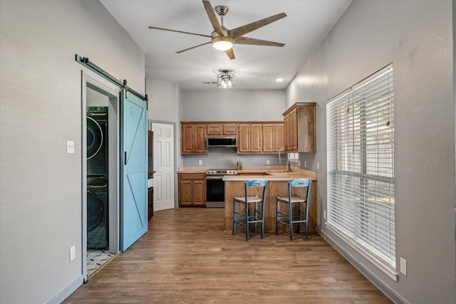 kitchen with stacked washer and clothes dryer, a kitchen breakfast bar, a barn door, kitchen peninsula, and stainless steel appliances