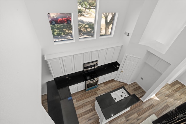 kitchen featuring white cabinetry, dark hardwood / wood-style flooring, a high ceiling, and appliances with stainless steel finishes