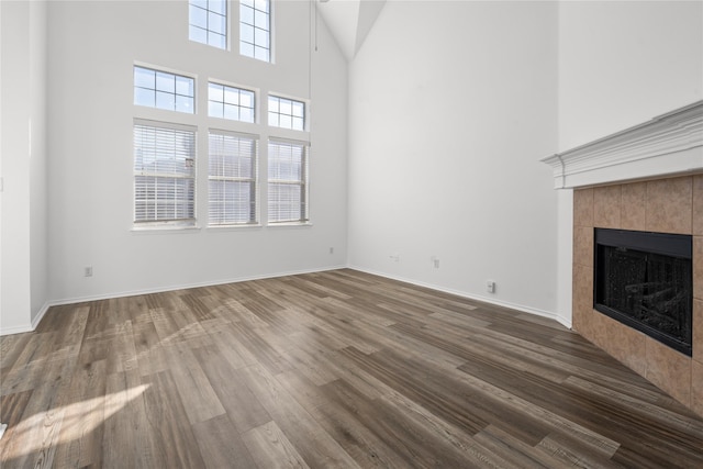 unfurnished living room featuring a tile fireplace, wood-type flooring, and a towering ceiling