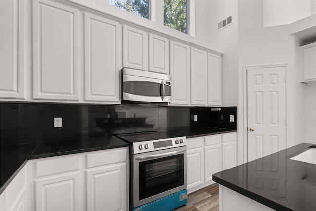 kitchen with a high ceiling, decorative backsplash, dark hardwood / wood-style flooring, white cabinetry, and stainless steel appliances