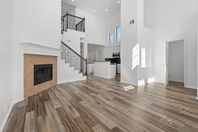 unfurnished living room featuring a fireplace, a towering ceiling, and wood-type flooring