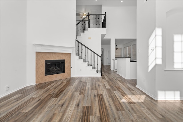 unfurnished living room with a fireplace, ceiling fan, hardwood / wood-style floors, and a high ceiling