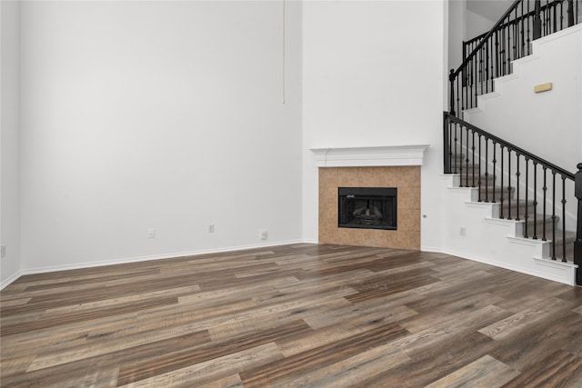 unfurnished living room with a fireplace, a towering ceiling, and dark wood-type flooring