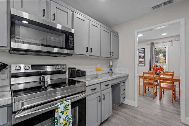 kitchen featuring gray cabinets, light stone counters, light hardwood / wood-style flooring, and stainless steel appliances