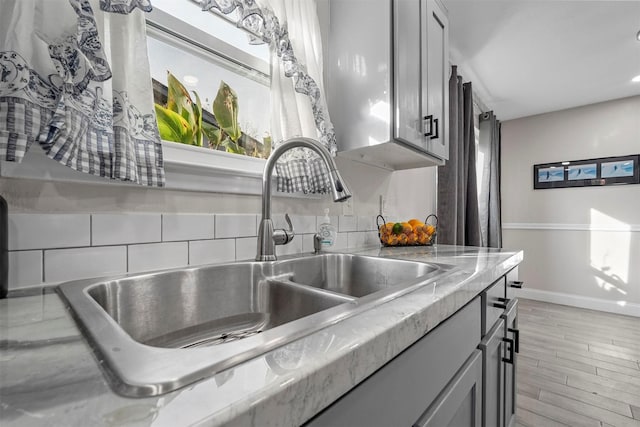 kitchen featuring gray cabinets, light hardwood / wood-style floors, light stone counters, and sink