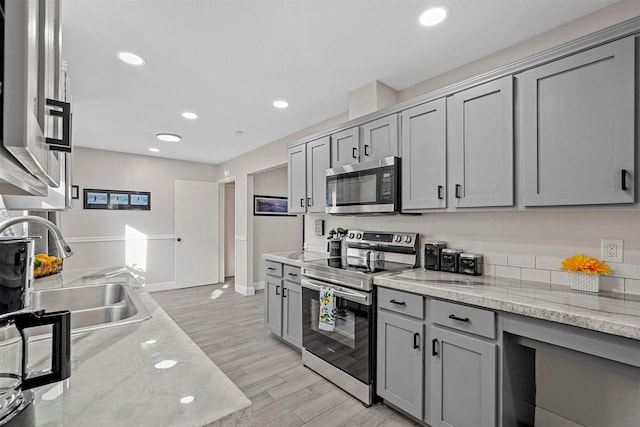 kitchen featuring sink, light hardwood / wood-style flooring, gray cabinets, appliances with stainless steel finishes, and light stone counters