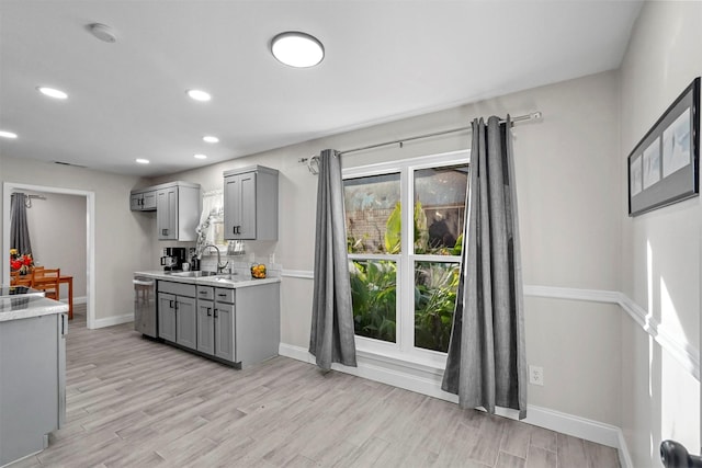 kitchen with gray cabinetry, stainless steel dishwasher, sink, and light hardwood / wood-style flooring