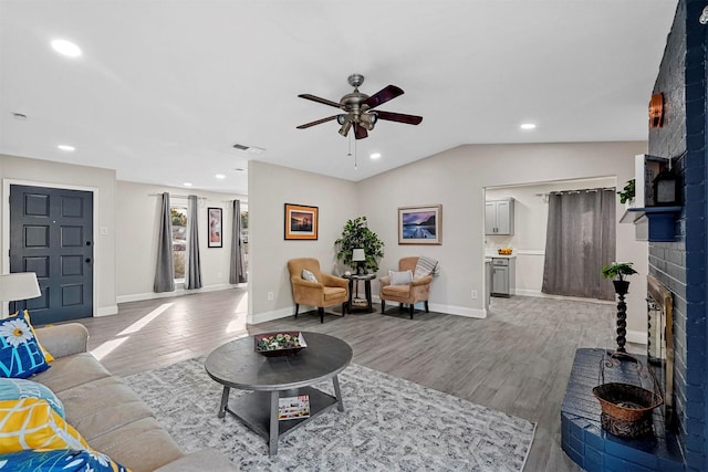 living room featuring hardwood / wood-style floors, vaulted ceiling, ceiling fan, and a brick fireplace