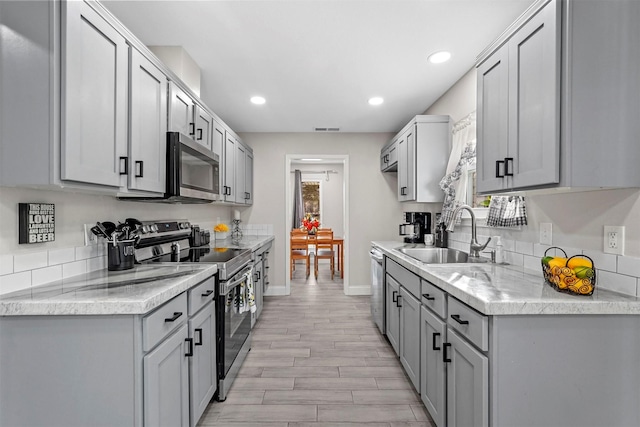 kitchen with gray cabinetry, sink, stainless steel appliances, and light hardwood / wood-style flooring