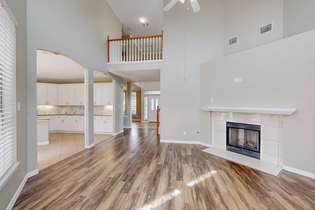 unfurnished living room featuring ceiling fan, light hardwood / wood-style floors, a tile fireplace, and high vaulted ceiling