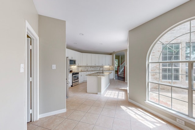 kitchen featuring appliances with stainless steel finishes, backsplash, sink, white cabinetry, and an island with sink