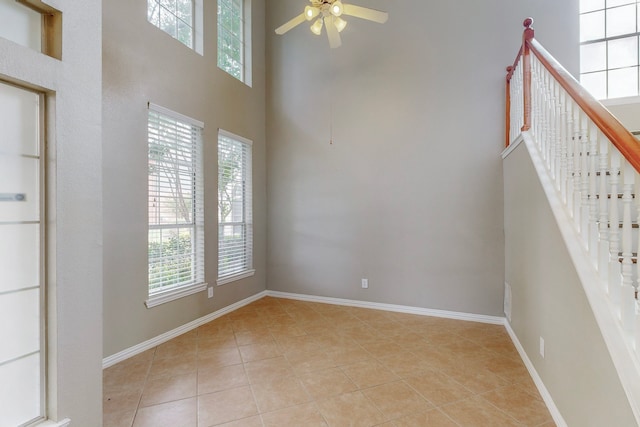 unfurnished room with ceiling fan, light tile patterned flooring, and a towering ceiling