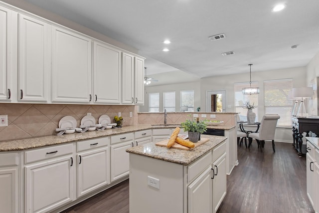 kitchen with dark wood-type flooring, sink, decorative light fixtures, white cabinetry, and a kitchen island