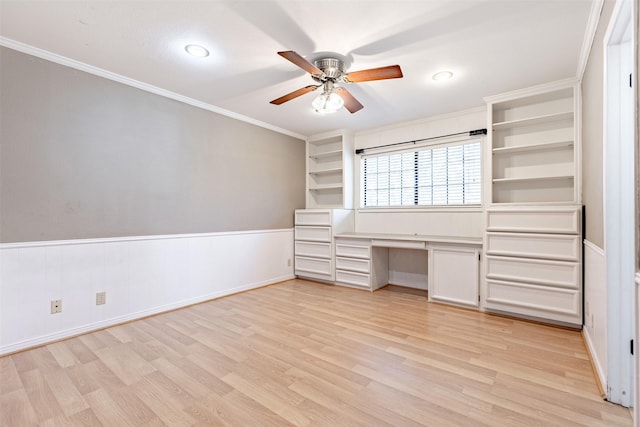 unfurnished office featuring crown molding, built in desk, light hardwood / wood-style floors, and ceiling fan