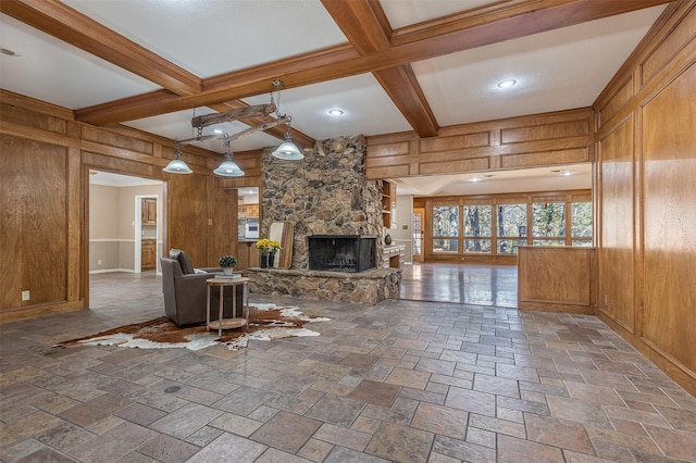 unfurnished living room with beamed ceiling, a stone fireplace, coffered ceiling, and wood walls