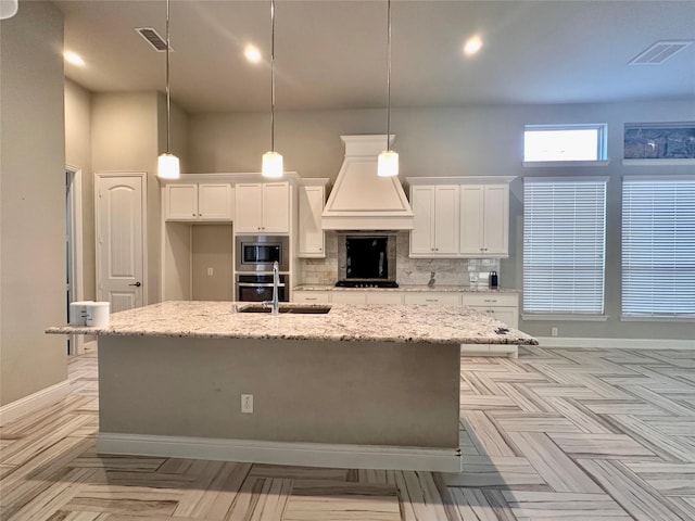 kitchen featuring white cabinets, an island with sink, tasteful backsplash, decorative light fixtures, and stainless steel appliances