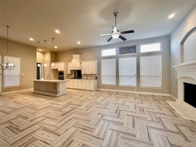 kitchen with white cabinets, pendant lighting, light parquet flooring, and an island with sink