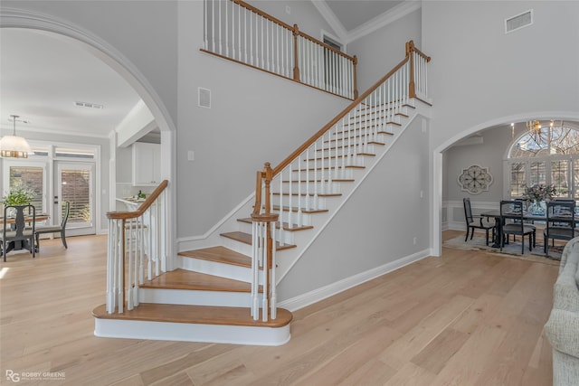 staircase featuring hardwood / wood-style flooring, a towering ceiling, ornamental molding, and an inviting chandelier