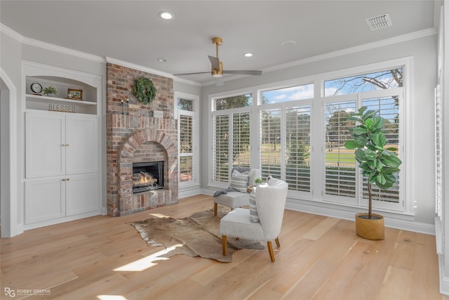 living room with crown molding, ceiling fan, a fireplace, and light hardwood / wood-style floors