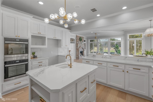 kitchen featuring hanging light fixtures, an island with sink, sink, and white cabinets