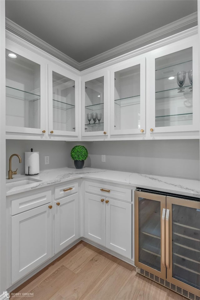 bar with sink, white cabinetry, light stone counters, beverage cooler, and light hardwood / wood-style floors